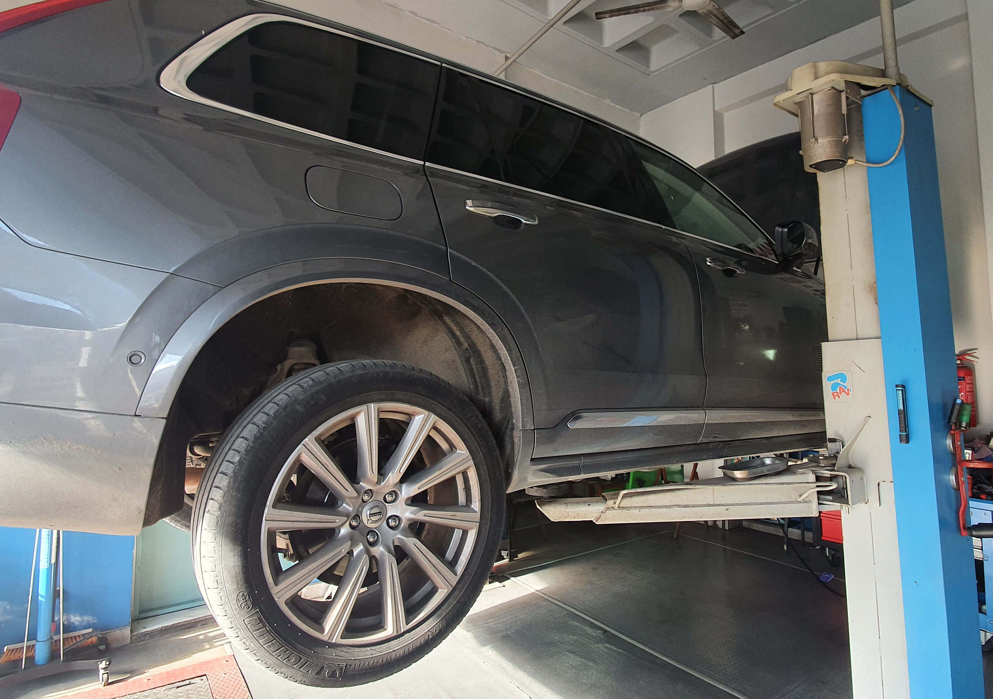 Ενα σύγχρονο SUV μάρκας VOLVO βρίσκεται σηκωμένο με τη βοήθεια αναβατορίου. Κεντρικά στο πλάνο βρίσκεται η πίσω δεξιά ρόδα και ανάμεσα στις ακτίνες της ζάντας φαίνεται το δισκόφρενο.