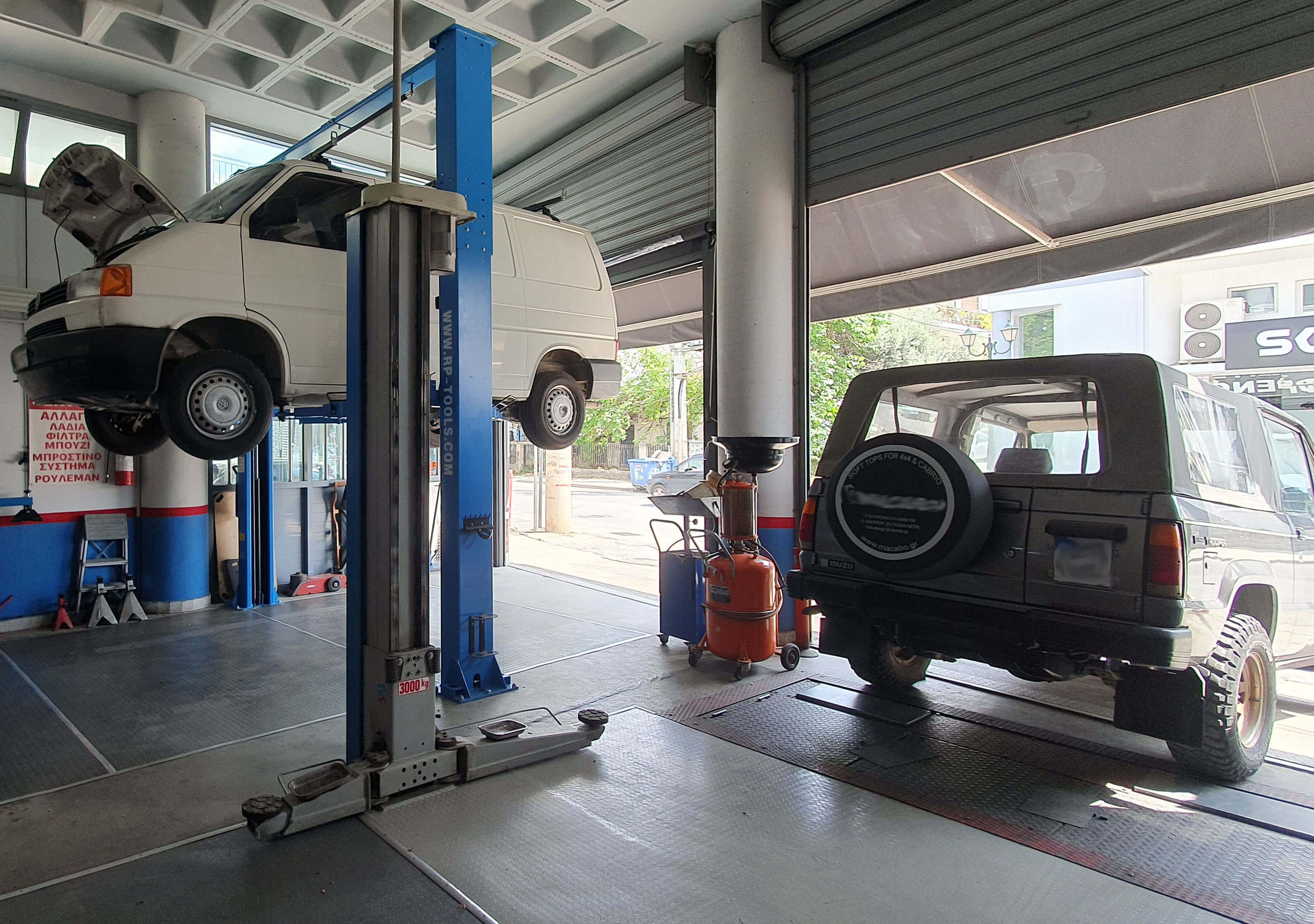 Εσωτερικό του εξειδικευμένου συνεργείου φρένων 'Φρενοδιάγνωση'. Ένα λευκό βανάκι είναι ανυψωμένο στο αναβατόριο δεξιά και ένα τζιπάκι είναι στη δεξια πλευρά του συνεργείου.